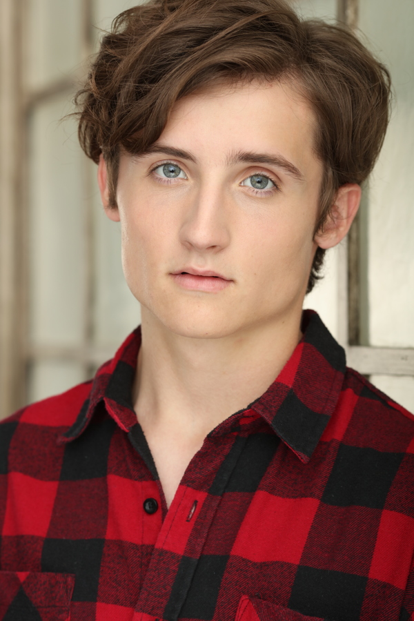 A young person with curly hair wearing a red and black flannel shirt, looking directly at the camera.